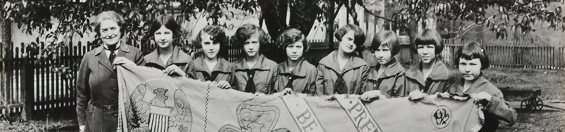  Eight Girl Scouts standing next to Juliette Gordon Low holding a Girl Scout banner.  