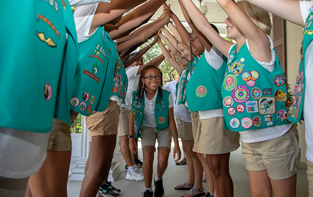 group of young girl scouts form a bridge with their arms as a one girl scout goes through