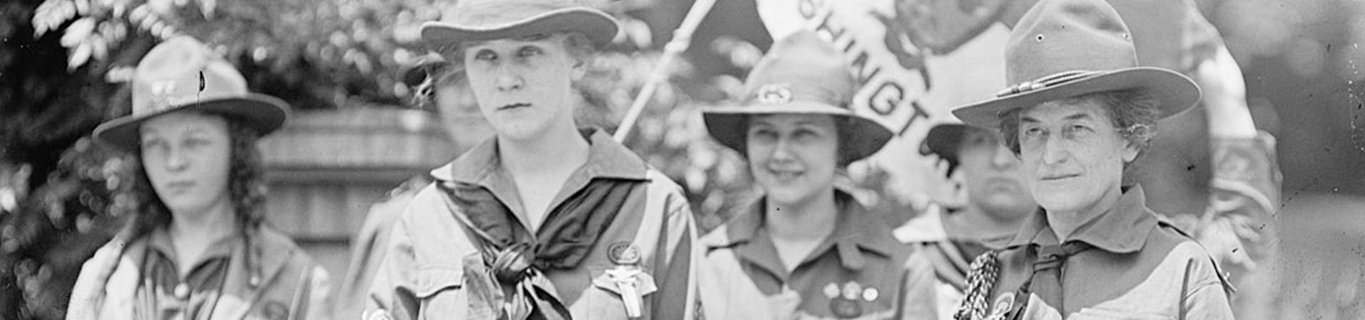  Early girl scouts holding a girl scouts flag with Juliette Gordon Low standing on the far right. 