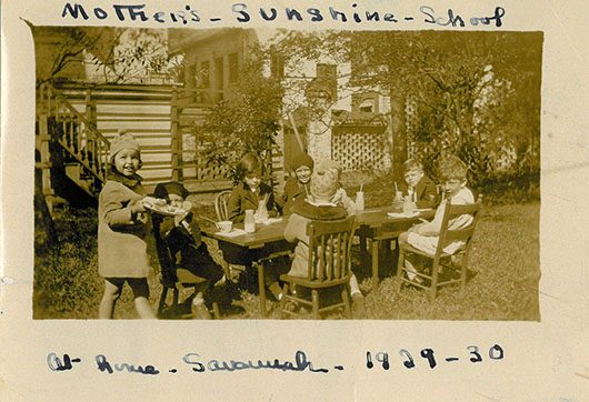 a group of small children smiling and sitting at a table in the garden of the birthplace