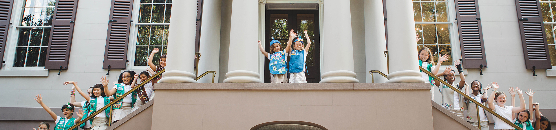  group of multi-level girl scouts with hands raised on the birthplace front steps 